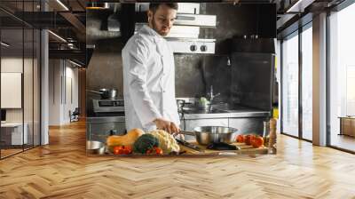 handsome young caucasian cook during the process of cooking. man in white uniform enjoy cooking in the kitchen, worker of restaurant. public catering concept Wall mural