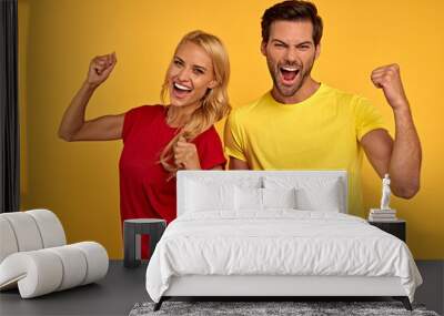 Joyful young couple two friends guy and girl in red and yellow casual clothes posing isolated on yellow wall background studio. People lifestyle concept. Mock up copy space. Doing winner gesture Wall mural