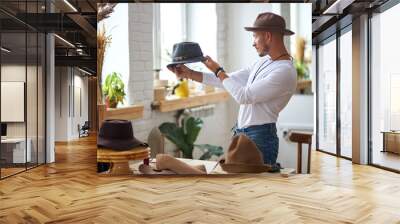 male hats maker standing at his atelier workshop, holding perfectly made hat for customers. successful adult business man employed at his own business Wall mural