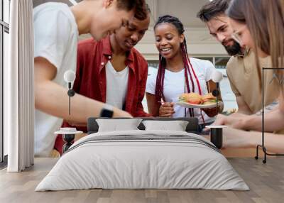 Multi-ethnic group of students playing table soccer, at barbecue outdoor party. Young happy excited friends playing table soccer football in garden terrace, going to eat burgers. Side view portrait Wall mural