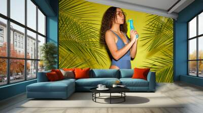 playful young european female in blue swimwear posing with water gun isolated over green wall background near green nature tropical plant. natural beauty, nature, sea, summer concept concept Wall mural