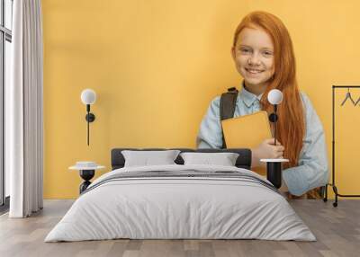 portrait of adorable smiling caucasian school girl with bag and book isolated over yellow background. 6 years old girl dream to go at school Wall mural