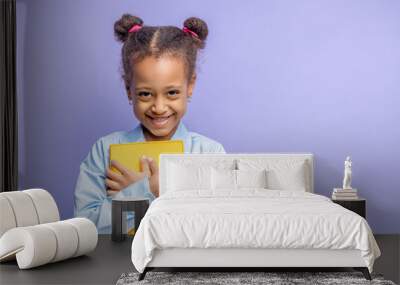 portrait of pretty little child with book isolated over purple background. happy girl with curly hair go in 1st grade at school.Back to school, elementary school Wall mural