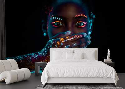 portrait of young beautiful african woman with fluorescent prints on face and closed mouth. fluorescent prints glowing on ultra violet rays, keep silence gesture Wall mural