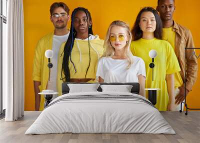 portrait of young confident caucasian woman with mixed race friends in the background, isolated on yellow studio background Wall mural