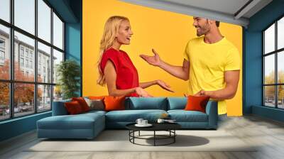 Side view of cheerful young couple two friends guy girl in casual clothes posing isolated on yellow background. People lifestyle concept. Mock up copy space. Looking at each other, speaking talking Wall mural