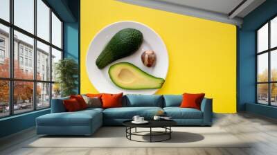 There are two slices of avocado on the plate. The fruit is divided into two parts. Next to it is an avocado seed. Yellow background color Wall mural