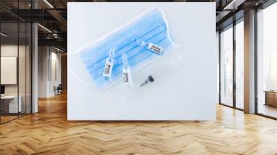 Vials of COVID-19 vaccines and a syringe for injection lie next to the medical mask Wall mural