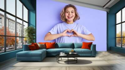 woman making heart from fingers and showing it at camera, expressing love. joyful excited female full of positive emotions, isolated on purple background Wall mural