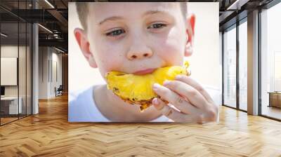 Cute Caucasian baby boy eating fresh pineapple outside in the summer heat. Wall mural