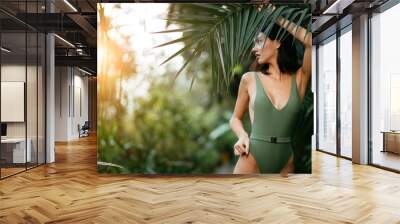 young attractive charming model around green fresh plants, slim slender female with short dark hair, posing at camera wearing green beautiful swimsuit or bikini. people and nature Wall mural