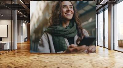 young attractive smiling broadly woman wearing light-colored coat and green scarf, walking city stre Wall mural