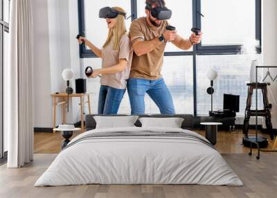 Young beautiful caucasian couple playing video games in virtual reality glasses. Funny Man and woman wearing virtual reality goggles for mazing experience in abstract vr world, at home in living room Wall mural