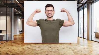 Young strong man in glasses and casual t-shirt showing biceps Wall mural