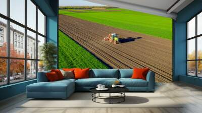 Aerial view of tractor as dragging a sowing machine over agricultural field, farmland Wall mural