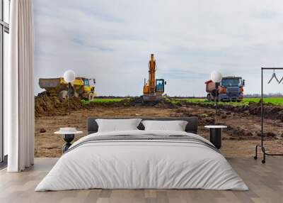 Big excavator is loading two trucks with ground on building site Wall mural