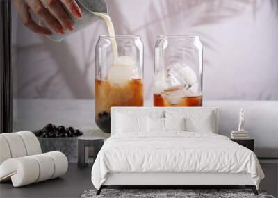 Female hand pouring milk into glass with black tea, ice cubes and cooked tapioca pearls for trendy bubble boba ice tea, two small grey ceramic bowls on marble board on grey concrete background Wall mural