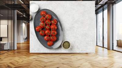 Roasted red tomatoes on branches on oval blue plate on grey background, top view, space for text Wall mural