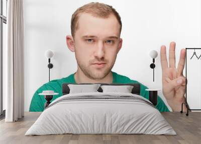 A funny young man in a green shirt shows three two Wall mural