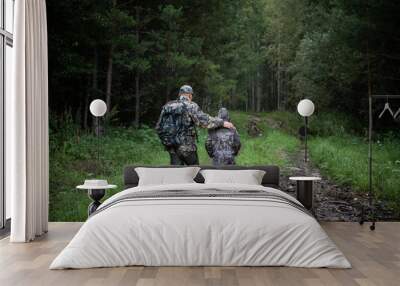 Hunters with hunting equipment going away through rural field towards forest at sunset during hunting season in countryside. Wall mural