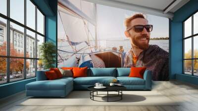 Man dressed in casual wear and sunglasses on a yacht. Happy adult bearded yachtsman close-up portrait. Handsome sailor on a boat smiling during regata on a sea or river. Wall mural