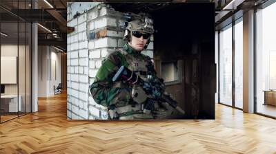 Military man with assault rifle standing inside building, he is ready for combat Wall mural