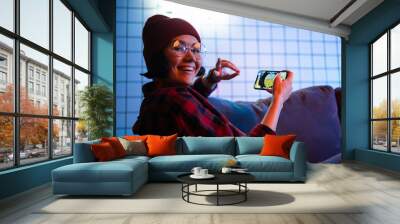 Teen girl exciting playing smart phone in a room lit with neon color at home. Wall mural