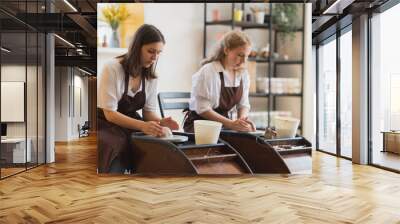 Two female ceramic artists in apron using clay material working in potter studio. Evening freelance distance learning. Adult hobby adventure. Winter educating leisure. Training in modern workshop. Wall mural