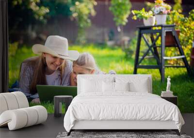 Woman and little girl laying on the spring flower field outdoors - having fun using a laptop Wall mural