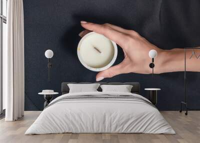 Woman hand holds a decorative scented candle on a black background Wall mural