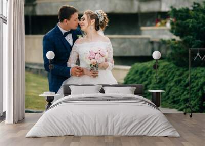 A kiss of a stylish bride and groom in a gorgeous dress and with a chic hairstyle. The man reaches out to kiss his beloved. Wall mural