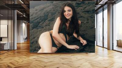 Beautiful sexy girl with long hair lying on beach with black sand. Young woman enjoys relaxing near ocean Wall mural