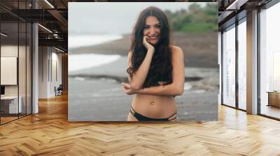 Portrait of happy girl with beautiful smile in swimsuit posing on black sand beach Wall mural