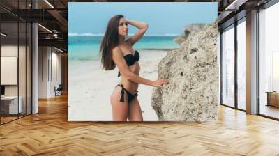 Sexy brunette girl in a swimsuit sunbathes on the white sand beach. Wall mural