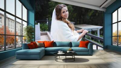 The bride dressed in Greek style wears a lalicik walks in the fresh air, poses near the forged balcony railing, smiles broadly. Wall mural