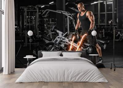 Handsome muscular man is doing battle rope exercise while working out in gym Wall mural