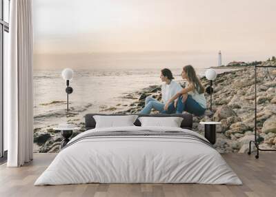 Mom and her teenage daughter relaxing together over sunset sea view Wall mural