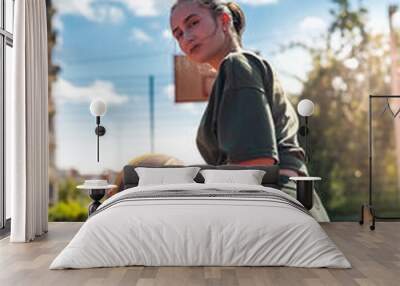 Attractive  young slim woman posing sitting on a basketball court holding a basketball Wall mural