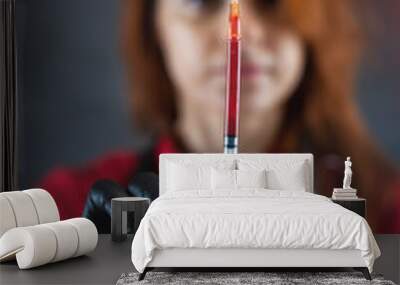 female doctor wearing red uniform medical gloves holding a syringe with blood isolatedon black Wall mural