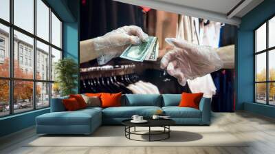 the buyer in plastic gloves gives the buyer dollars for the goods in the clothing store. coronavirus Wall mural