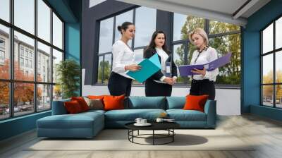 Three women in teamwork. They holding folders and discussing information outdoors Wall mural