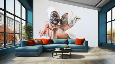 Two caucasian women wear towel having black clay facial mask isolated on white Wall mural