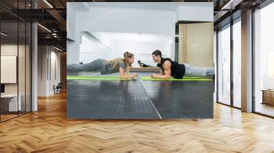 Two people in gym doing plank exercise together Wall mural