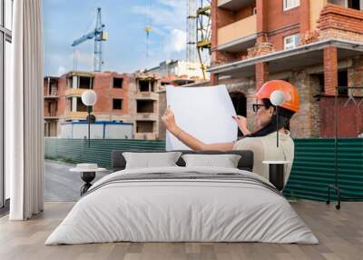 Woman architect in orange helmet with drawing near construction site Wall mural