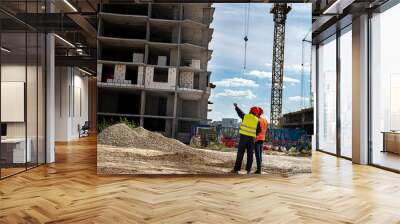 workers in special clothes and helmets stand near the construction of the house and the crane Wall mural