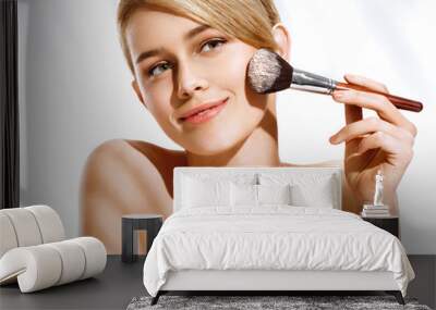 Woman applying powder on the face using makeup brush. Photo of blonde woman isolated on white background. Beauty concept Wall mural