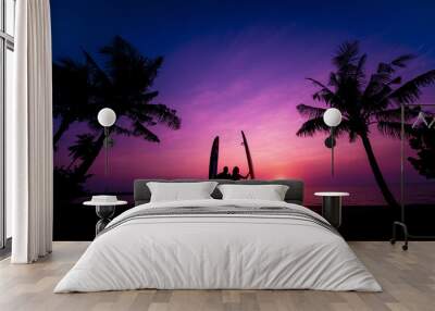 Silhouette of surfers couple holding long surf boards at sunset on tropical beach Wall mural