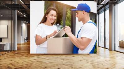 Young courier delivering goods to a young woman at home Wall mural