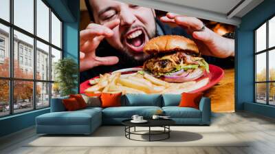 Young man eating a cheeseburger. Wall mural