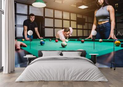 Young man trying to hit the ball in billiard. Wall mural